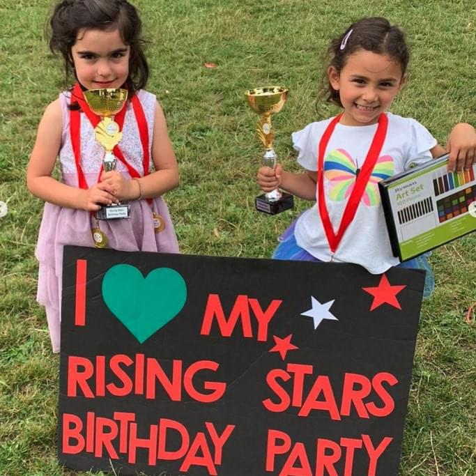 Young girls posing with Rising Stars birthday party sign