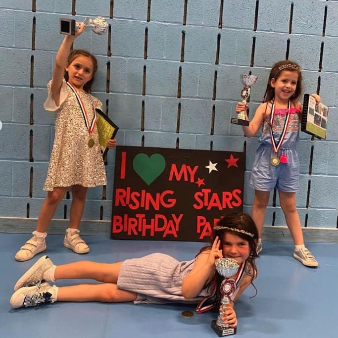 Three young gilrs posing with Rising Stars birthday party sign