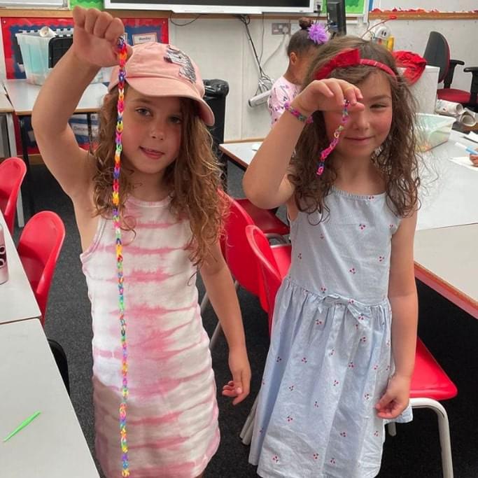 Two young girls holding up jewelry that they have made at a Rising Stars activities holiday camp in london
